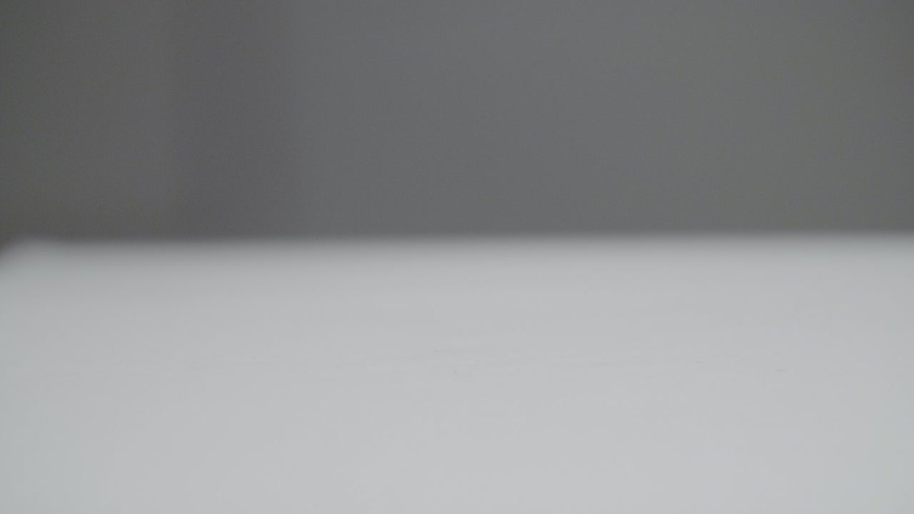 Slow Motion of a white plain sphere falling on a white surface and bouncing off. A dark gray background. Shot in Slow Motion in 4K. Shallow depth of field with fixed Focus