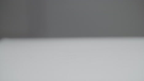 slow motion of a white plain sphere falling on a white surface and bouncing off. a dark gray background. shot in slow motion in 4k. shallow depth of field with fixed focus