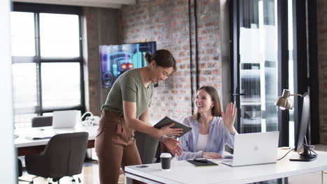 Young-Caucasian-woman-engages-in-a-cheerful-business-conversation-with-an-Asian-woman-in-an-office