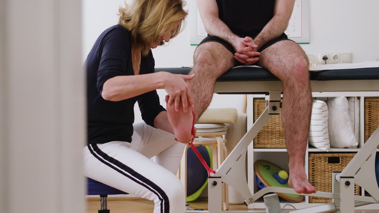 A shot of a professional female physiotherapist treating a sitting young, male patient with a resistance band