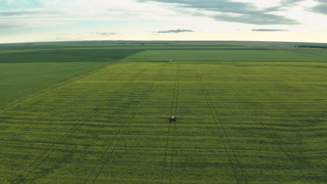 spectacular scenic aerial view of vast flat green farmland with single farming machine spraying fungicide on crops, saskatchewan, canada, high aerial pull back
