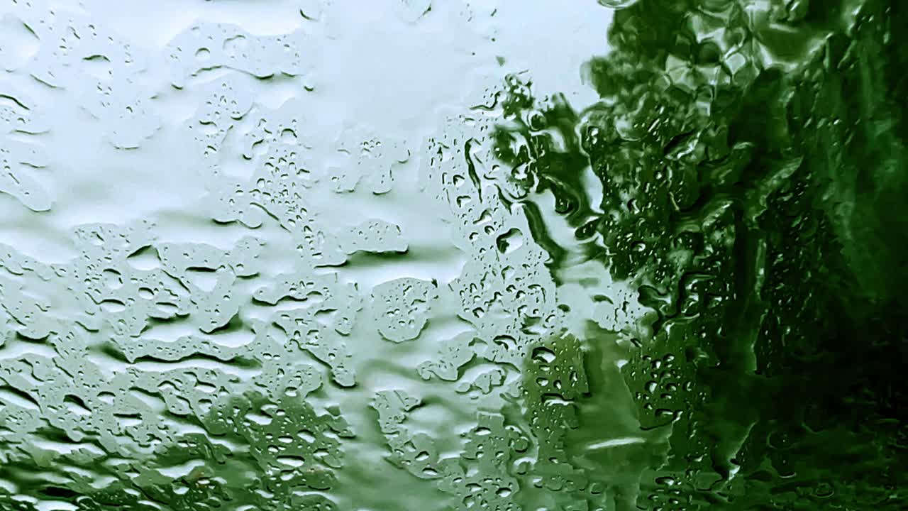 Low visibility for raindrops over windscreen while driving on highway with trees in background and wiper removing rain for bad weather