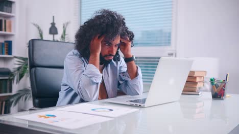 tired middle eastern man clutches his head while sitting in his office