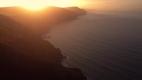 coastal aerial scene with bright colors of sunset over rugged coastline in exmoor devon with calm ocean waves below in bristol channel. drone rural english seaside footage 4k.