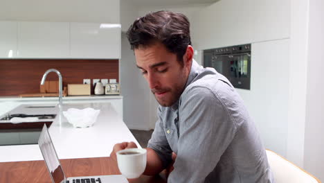 hombre guapo bebiendo café y usando una computadora portátil