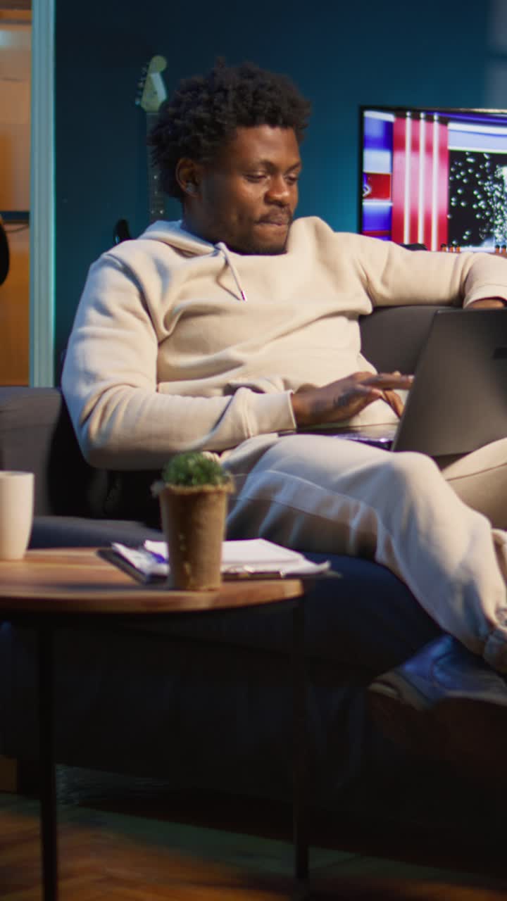 Afroamerikanischer Mann arbeitet am Laptop und trinkt Kaffee auf der Couch