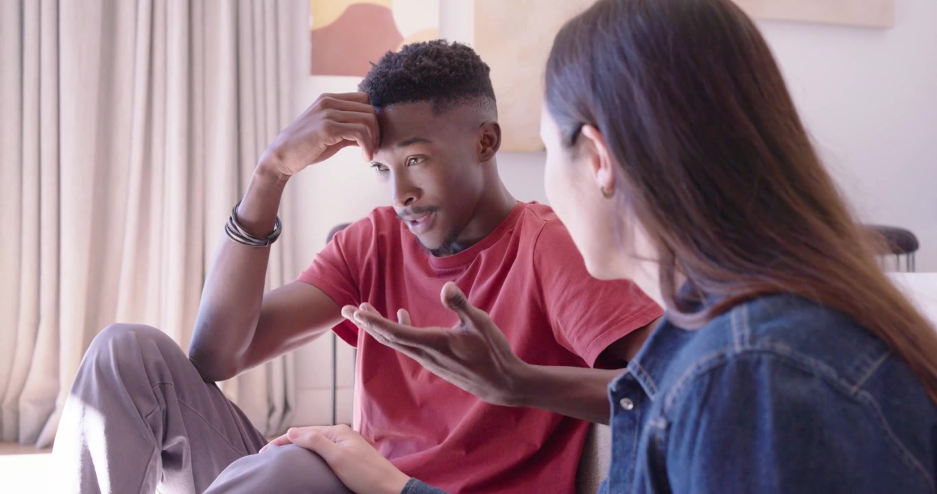 Diverse couple on sofa woman wearing denim speaking, African-American man rubbing head seeking calm