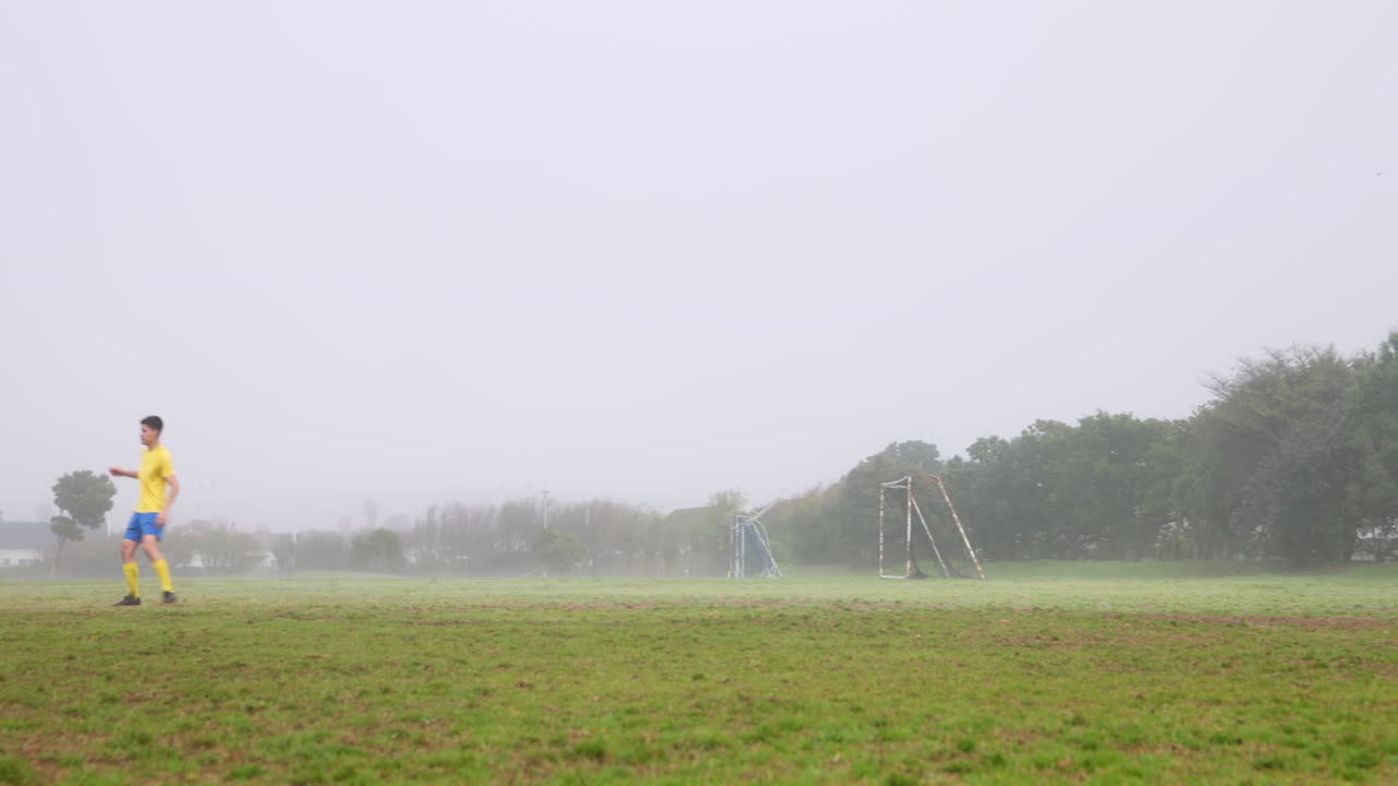 Playing soccer on foggy field, player kicking ball towards goalposts