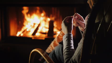 female hands with knitting needles - knits warm clothes sitting by the fireplace