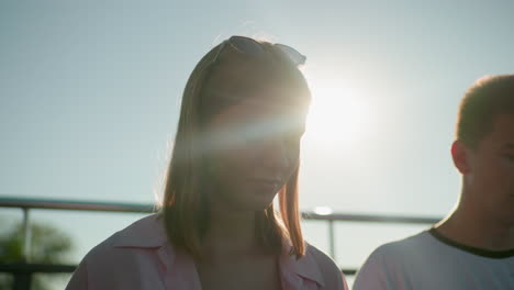 sunlit silhouette of lady with glasses on her head talking to a colleague outdoors, soft glow around her head, iron railing in background