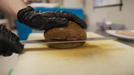 chef using the knife to cut in half the wholemeal bread for a burger