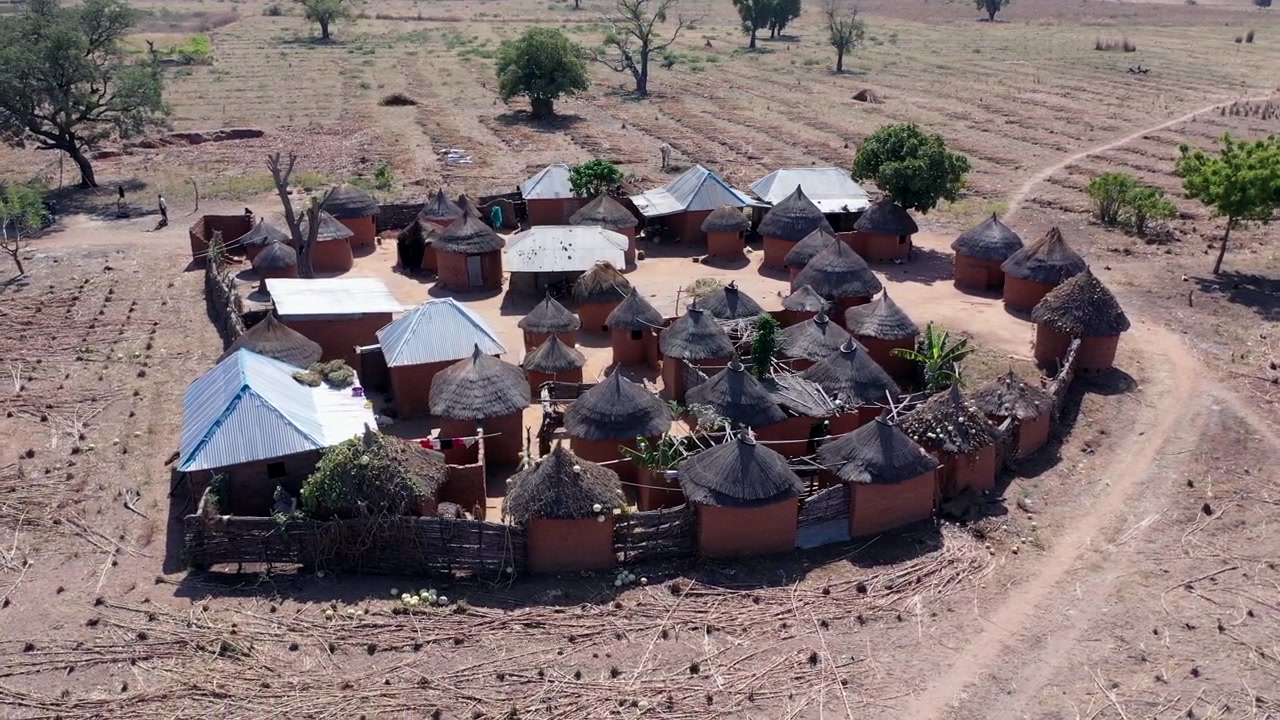 Sekelompok rumah dengan atap jerami rumput di desa pertanian tradisional di Nigeria - tampilan udara mengorbit.