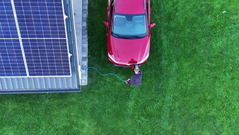 aerial view of man plugging electric car at home with solar panels. clean energy and sustainable living concept