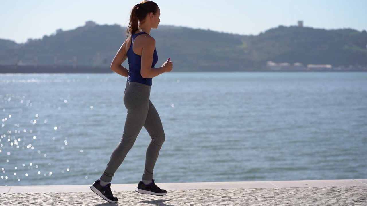 Side view of sporty young woman jogging along embankment