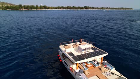 Yate-Catamarán-Navegando-En-El-Mar-Azul-Cerca-De-Las-Islas-Gili-Con-Una-Mujer-Joven-En-Traje-De-Baño-En-La-Azotea-Del-Barco---Retroceso-Aéreo