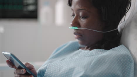 Black-woman-Patient-in-Hospital-with-Saline-Solution-Volumetric-Infusion-Pump-using-mobile-phone-on-examination-couch.-African-women-lying-in-hospital-bed-with-smart-mobile-phone-while-in-hospital.