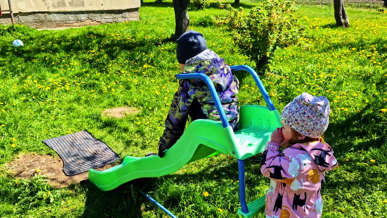 Children playing on slide in grassy yard with dandelions and sunshine