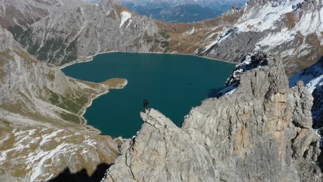 rotating drone shot of a man standing on a cliff overlooking love heart lake in switzerland after a long, intense and extreme hike to reach the top of the mountain