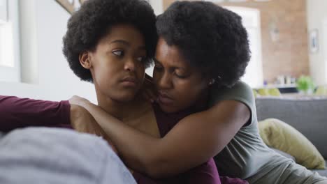 sad african american mother and daughter sitting on sofa, embracing