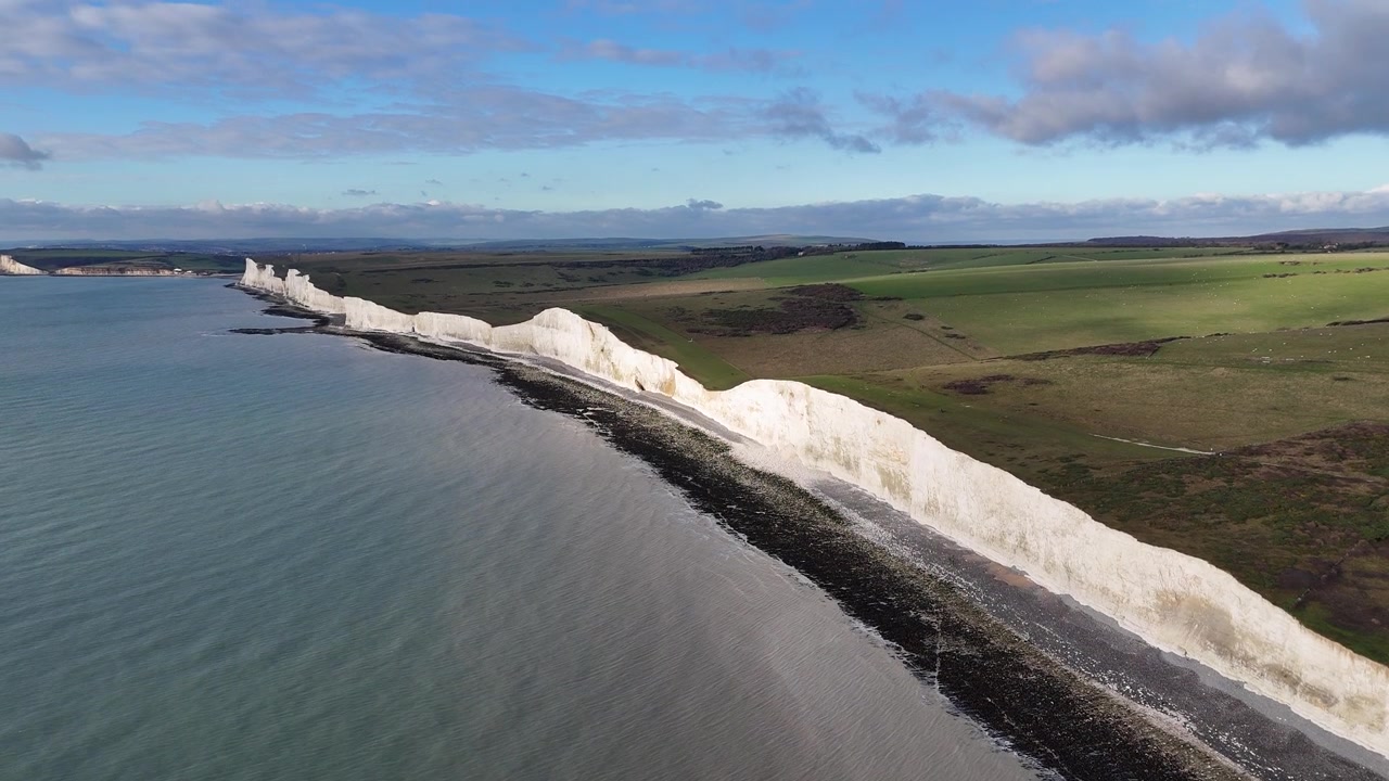 Gündüz Doğu Sussex İngiltere'de sakin denizin ve yeşil kırsalın yanında engebeli sahil şeridi boyunca beyaz tebeşir oluşumlarıyla Seven Sisters Kayalıkları'nı gösteren havadan drone çekimi