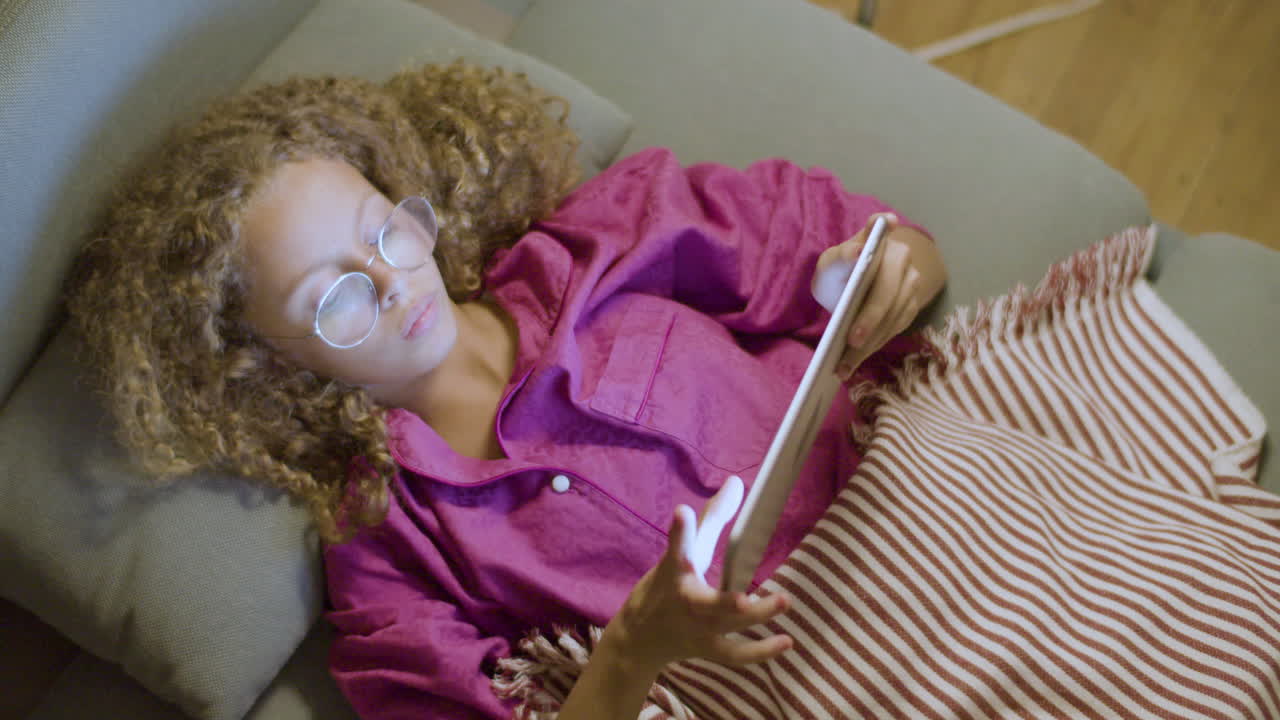 Cute blonde girl lying on couch using digital tablet