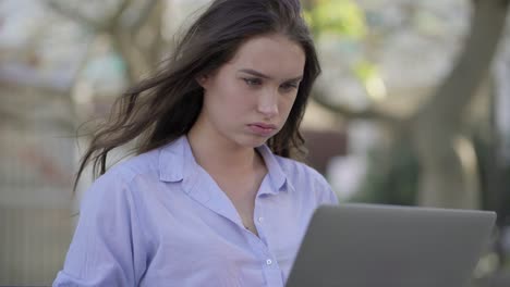 Mujer-Caucásica-Seria-En-El-Parque-Escribiendo-En-Una-Computadora-Portátil,-Luciendo-Cansada