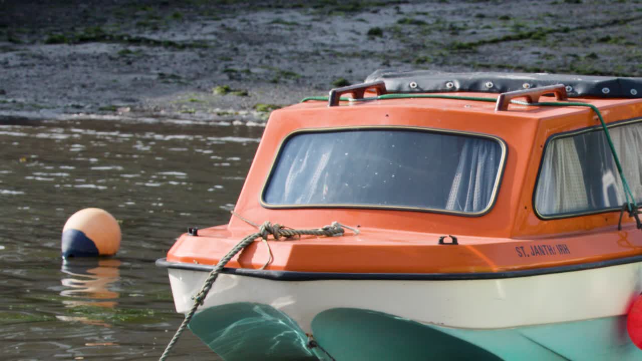 Orange and white motorboat drifts near buoy in calm, sunlit harbor at low tide
