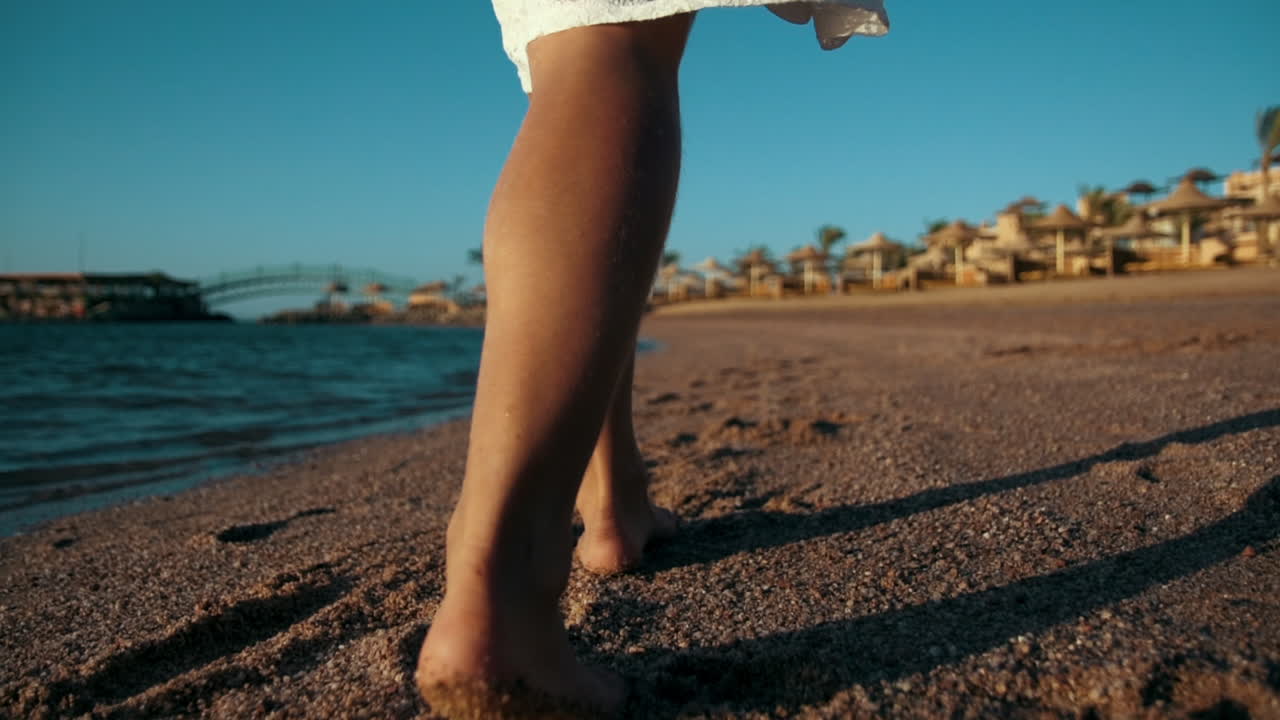 Gambe di giovane donna che camminano lungo la costa sabbiosa durante le vacanze estive.