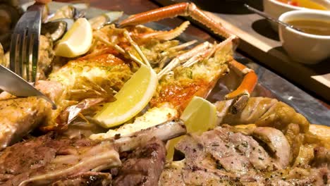 close-up of grilled seafood and meat platter with lemon wedges and dipping sauces.