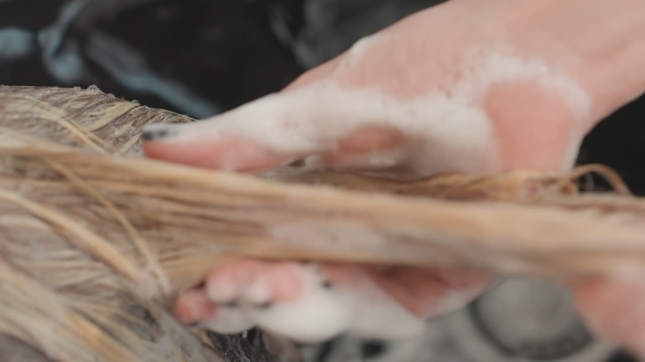 Stylist skyller og reder blondt hår med en sæbebehandling, nærbillede af hænder, der trækker gennem våde lokker for at fjerne produkt, synlig vask og håndklæde, professionel salon arbejdsgange og skarpt