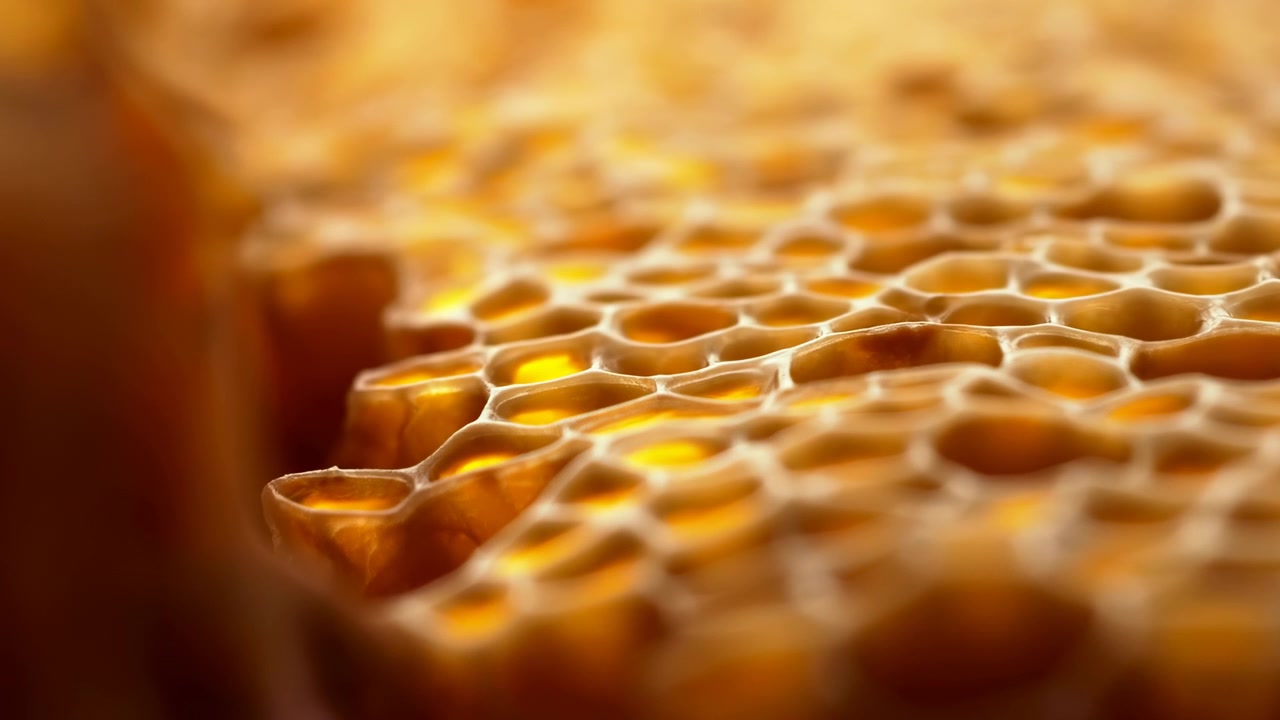 Primer plano de panal dorado con miel reluciente, iluminación ámbar cálida que resalta intrincadas celdas hexagonales.
