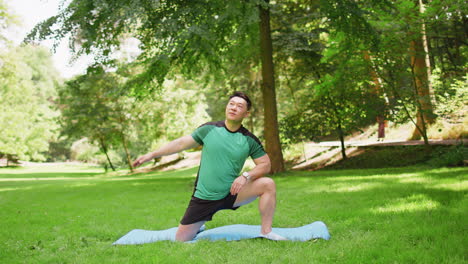 Adult-Asian-sportsman-guy-does-gymnastics-practices-yoga-performs-exercises-on-mat-in-city-park