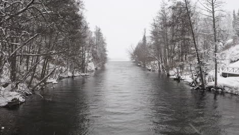 aerial shot of a small river stream by a lake in sweden during snowfall on a cold winter day