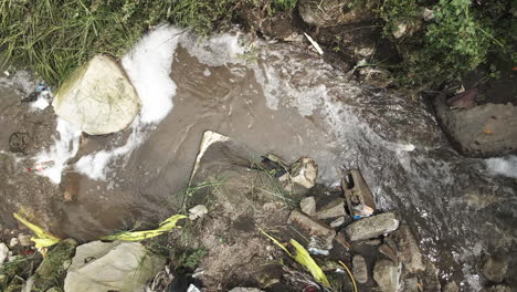 Static-top-down-aerial-footage-of-a-muddy-creek-with-litter-all-around-it