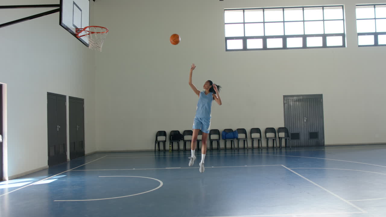 Playing basketball, woman shooting ball towards hoop in indoor court