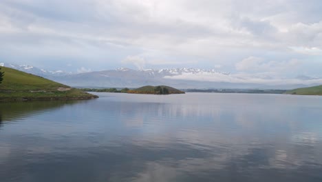 low drone flight over lake opuha, new zealand with snow-capped mountains in background