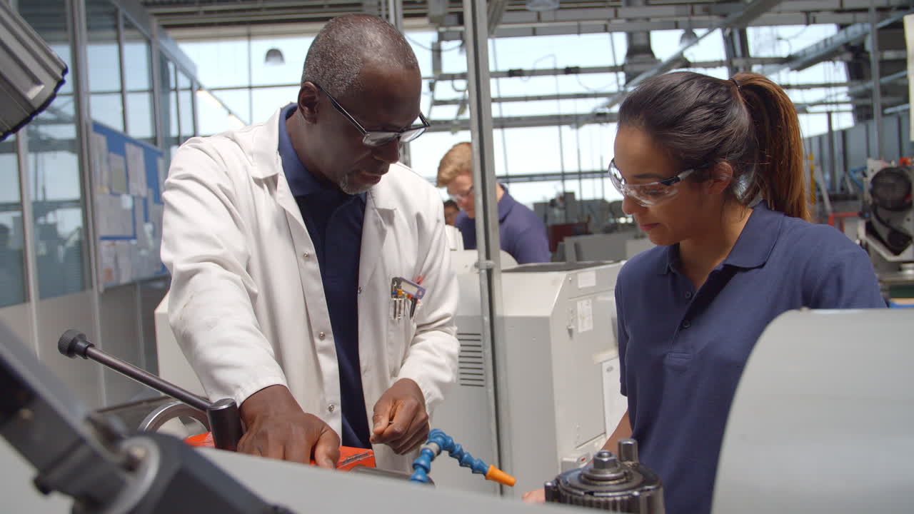 Engineer Teaching Apprentice How To Use Machine In Factory