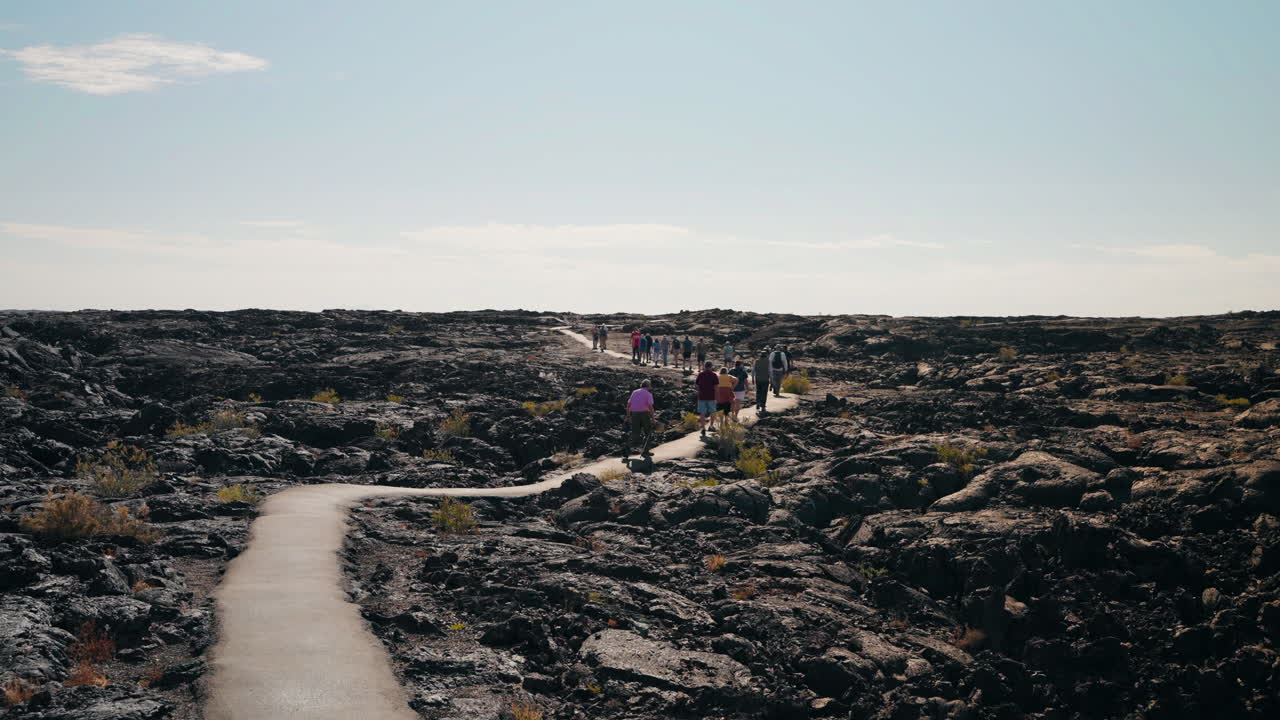 Group of people walking on a paved trail through a vast lava field