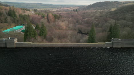 Flying-over-reservoir-dam-wall-to-reveal-winter-landscape-at-Haweswater-English-Lake-District-UK