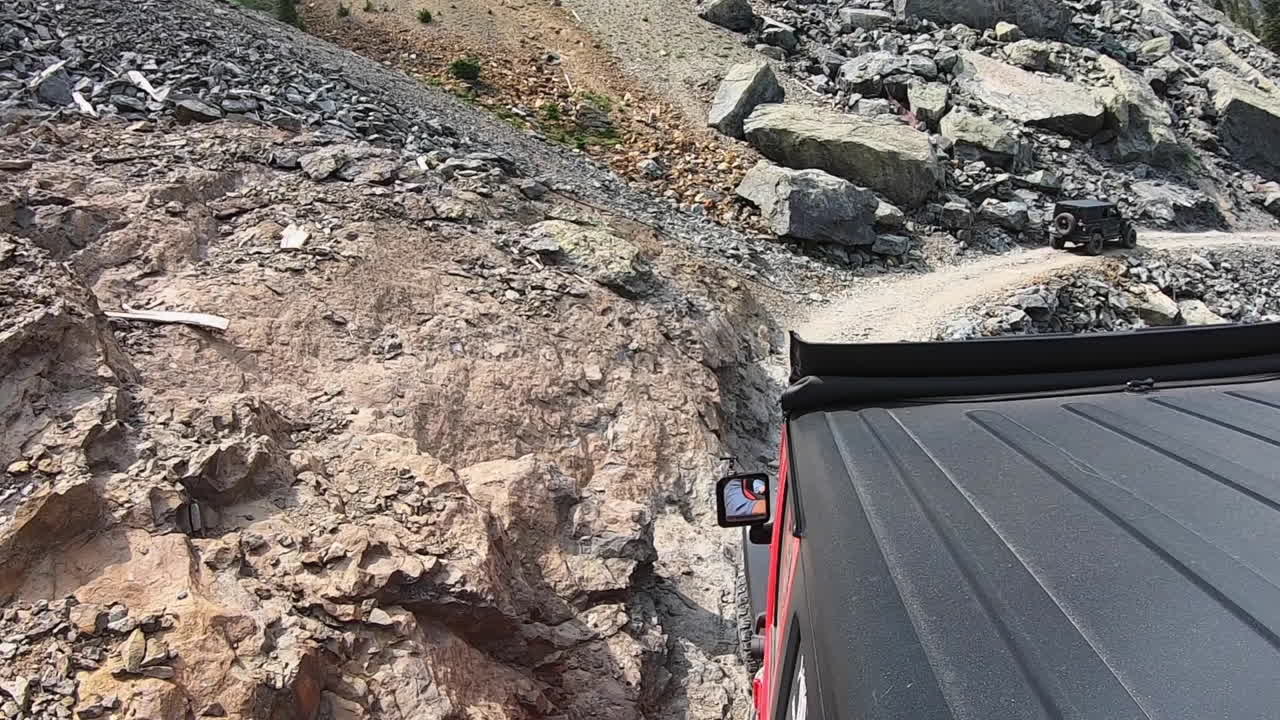 azotea de un vehículo 4wd siguiendo a otro en un estrecho sendero rocoso cortado en la ladera de la montaña con una caída total