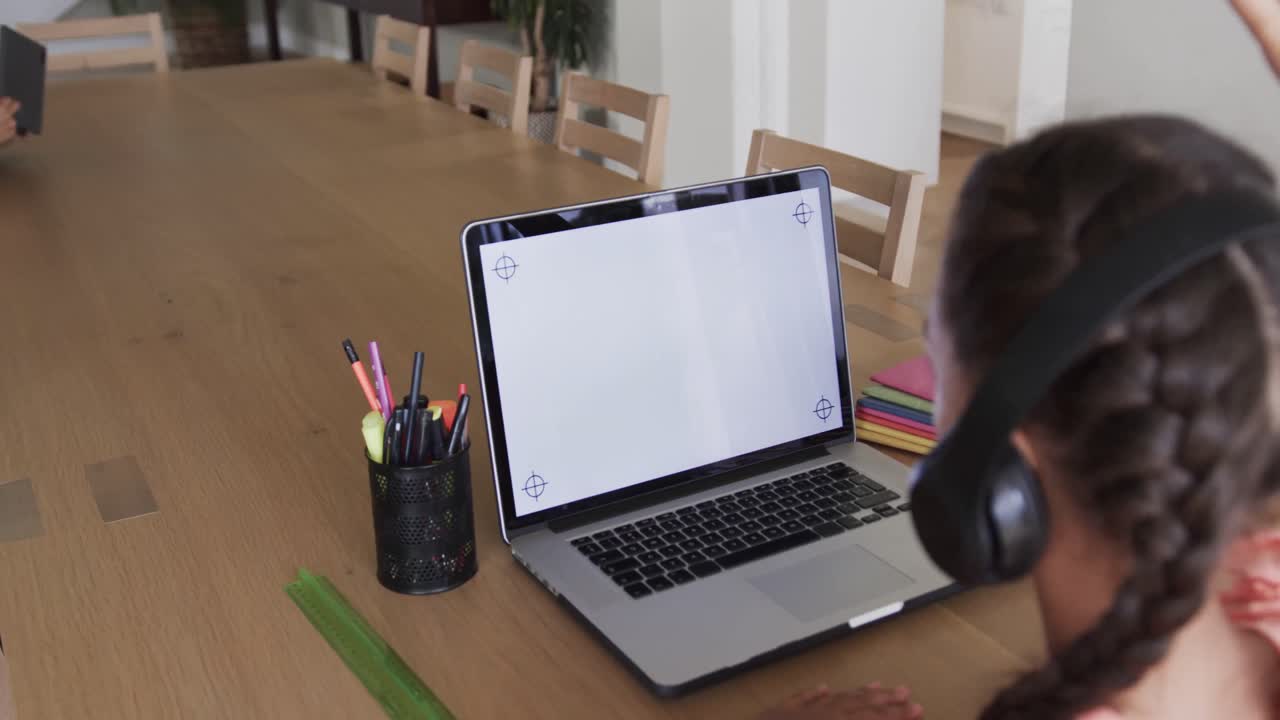 Biracial girl learning online at table using laptop with copy space on screen, slow motion