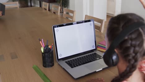 chica biracial aprendiendo en línea en la mesa usando portátil con espacio de copia en la pantalla, cámara lenta