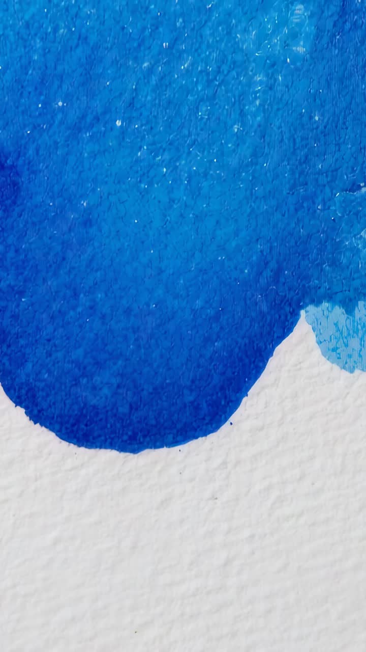 Vertical video: Filming blue watercolor drying on watercolor paper in studio showing grain, flecks