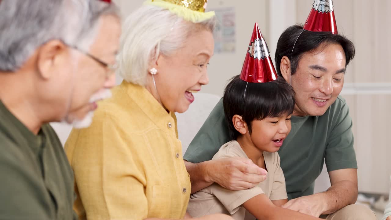 Multigenerational Asian family celebrates a birthday indoors, wearing party hats and sharing joyful smiles