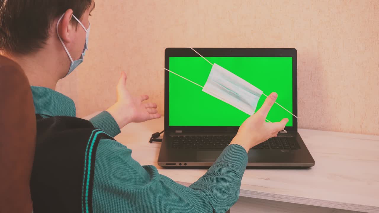 un hombre se pone una máscara de protección facial a sí mismo y al interlocutor por llamada de video y comienza a escribir en una computadora portátil, seguridad epidemiológica, trabajo remoto, pantalla verde