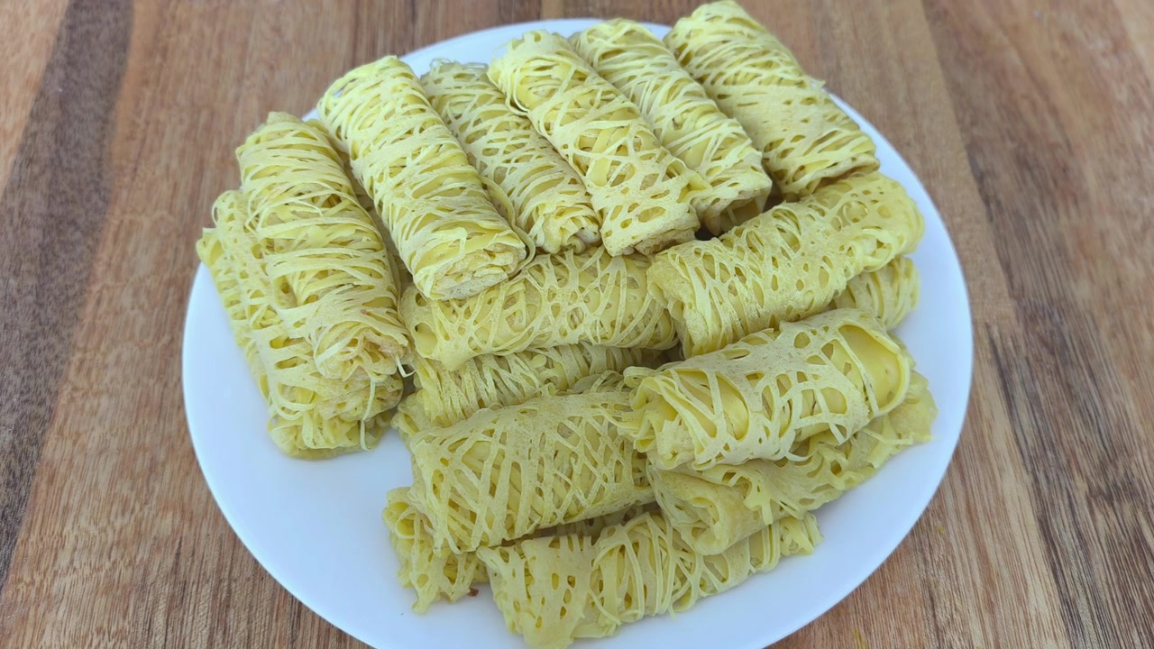 Várias crepes amarelas rendadas enroladas estão dispostas em um prato branco limpo. Este lanche tradicional malaio é conhecido como roti jala e servido com curry.