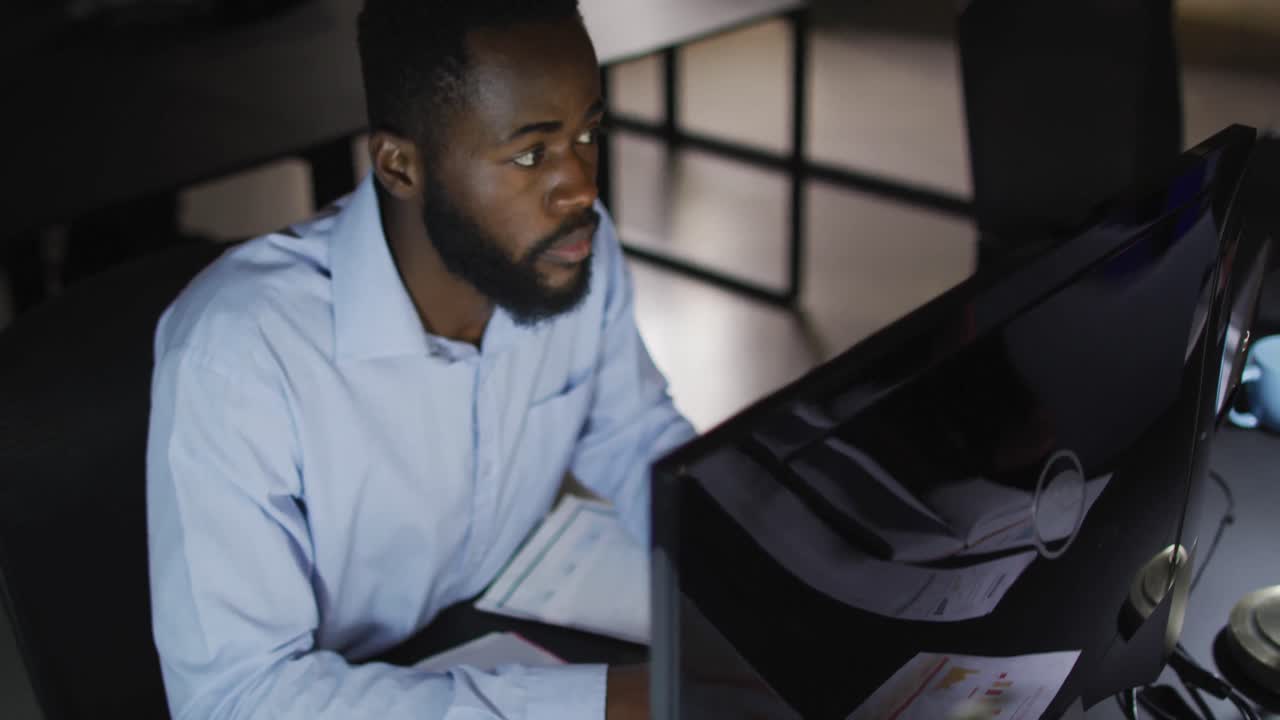 Video af afroamerikansk forretningsmand, der sidder ved skrivebord og bruger computer om natten på kontor.