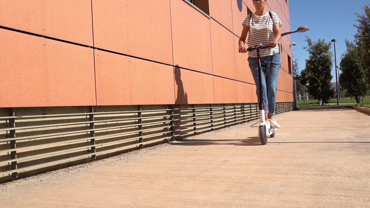 Žena jezdí po městě na elektrické koloběžce.