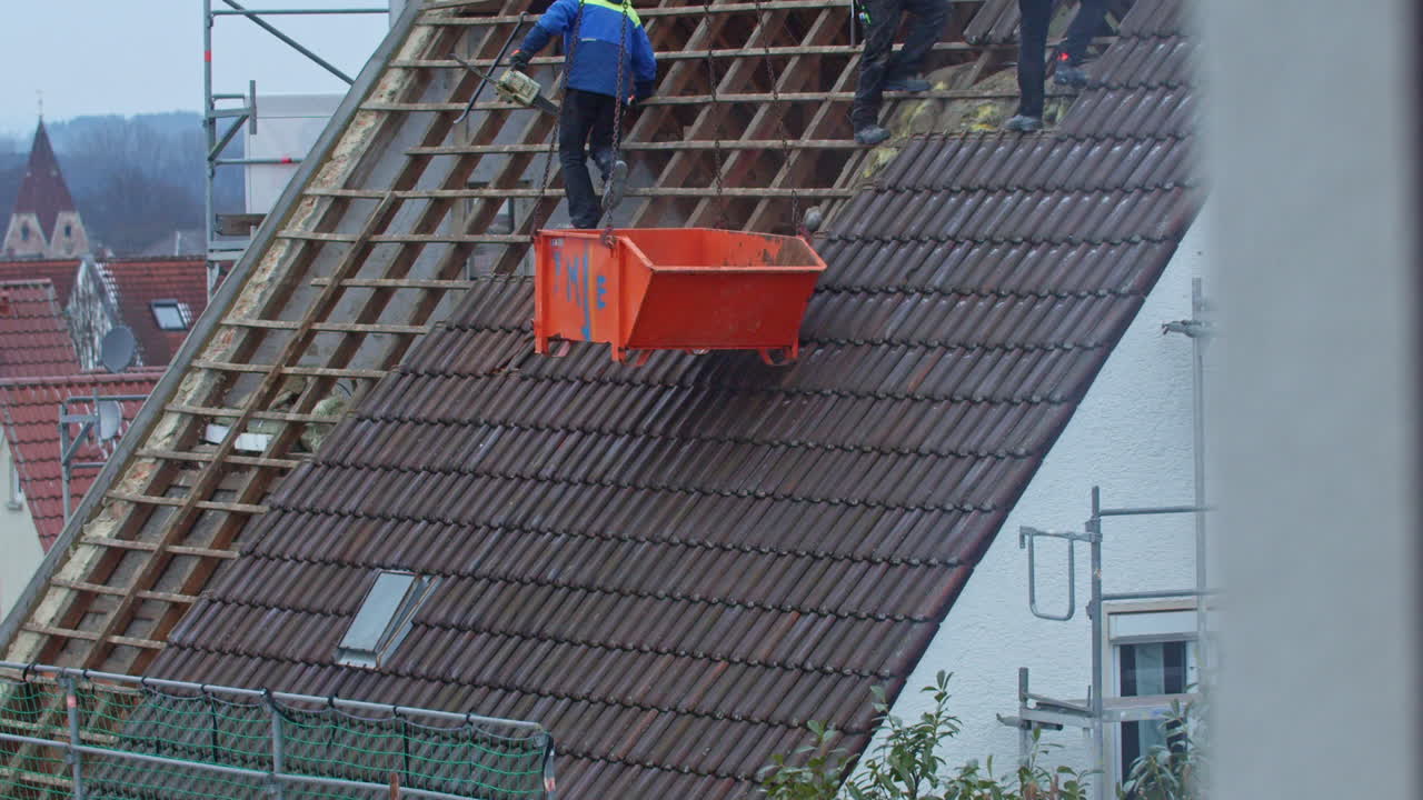Wide shot of an orange container getting lowered at the side of a roof