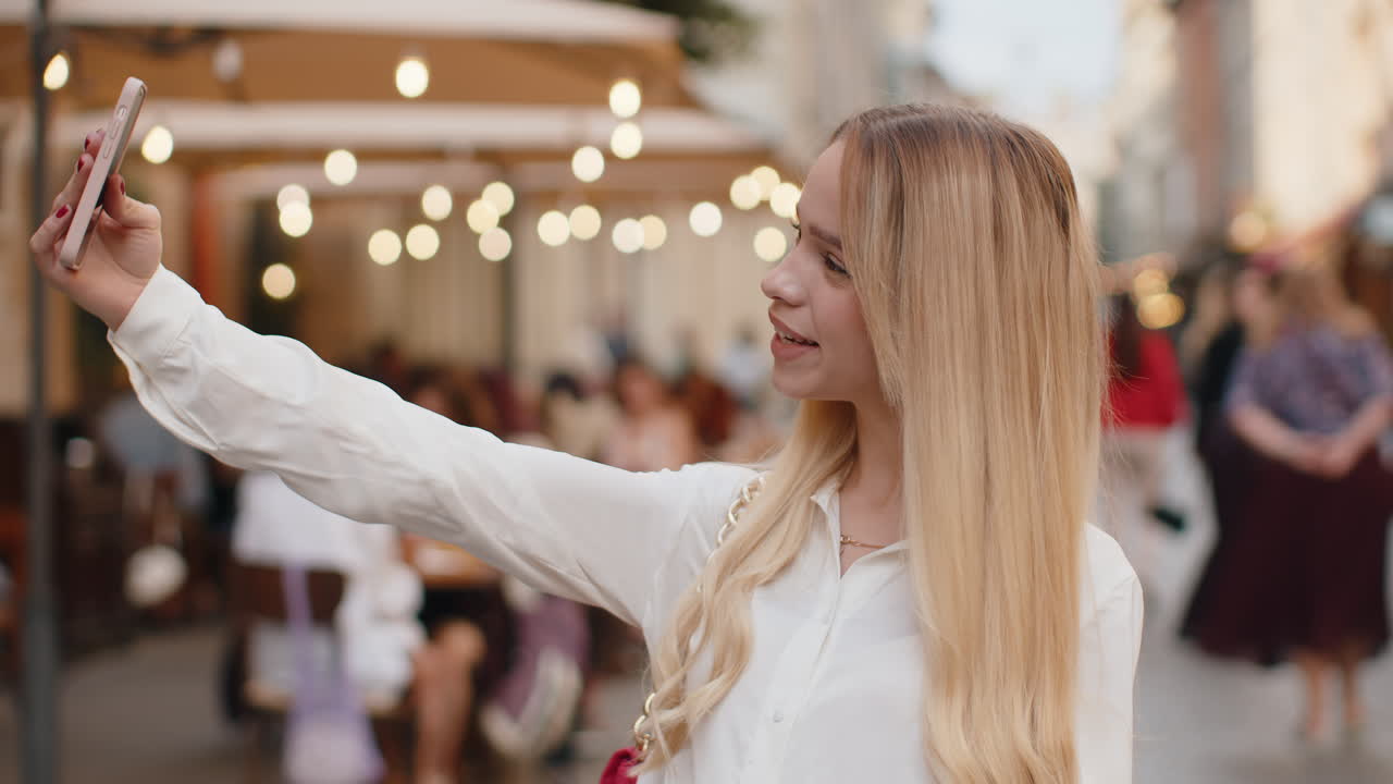 젊은 여성 블로거가 스마트 폰으로 셀카를 찍고 도시 거리에서 가입자와 온라인 동영상 통화를 하고 있습니다.